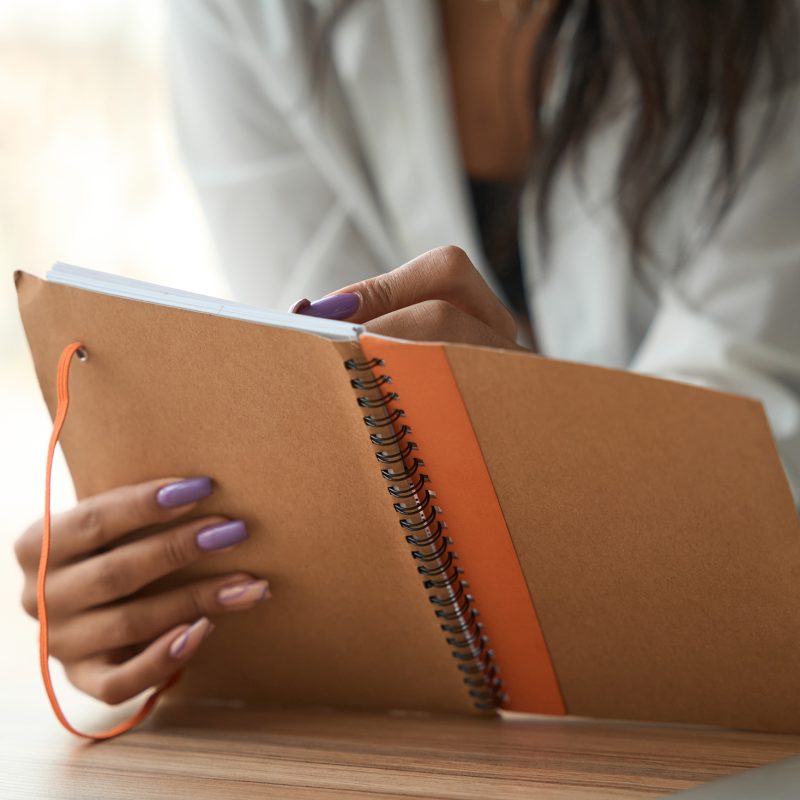 Cropped view of female with beautiful manicure holding and reviewing notebook indoors