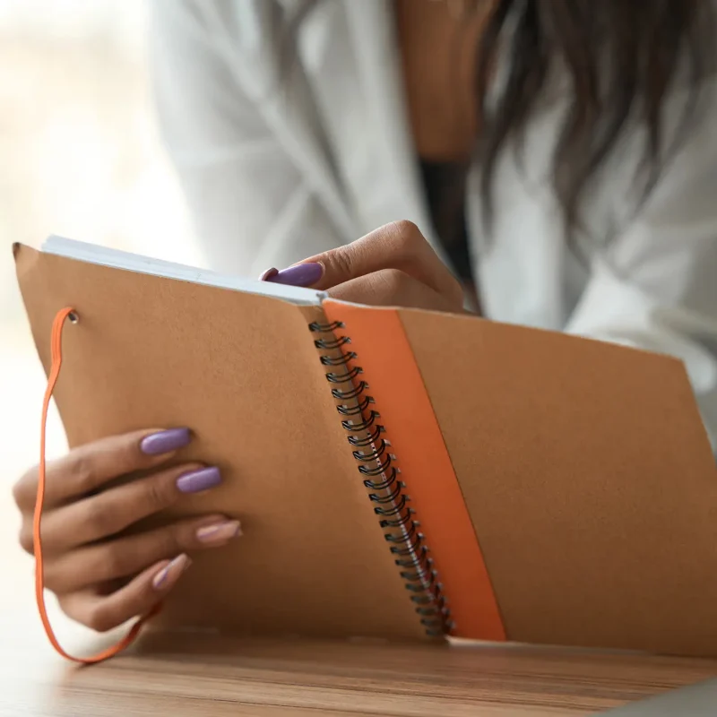 Cropped view of female with beautiful manicure holding and reviewing notebook indoors