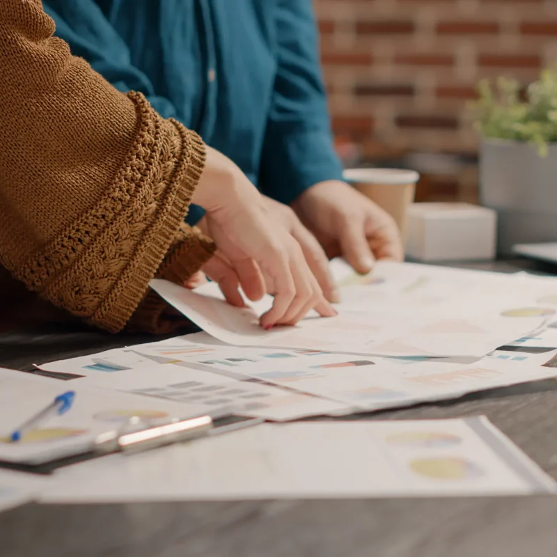 Close up of business people looking at papers with rate charts to plan project and presentation at desk. Colleagues working together with information files to design marketing strategy